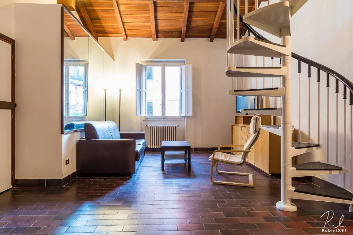 Salón con sofá, escalera de caracol hacia el altillo y ventana